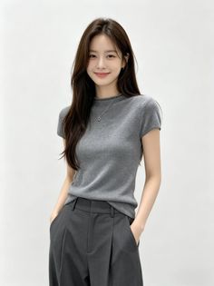 Woman with long dark hair wearing a gray t-shirt and gray pants, smiling at the camera