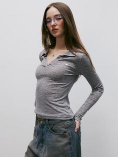 Woman with long hair and glasses wearing a gray long-sleeve top and jeans
