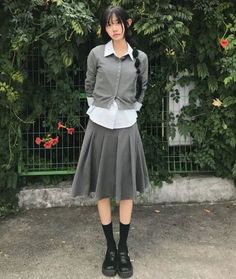 Person in a school uniform with braided hair standing outdoors against green foliage