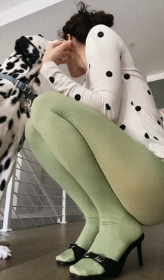 Person in polka dot shirt and green tights interacting with a dalmatian dog