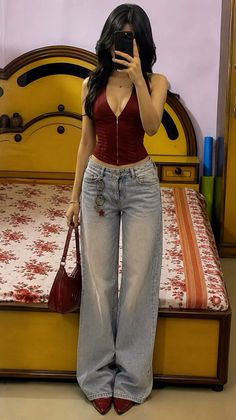 Woman in a red top and wide leg jeans taking a mirror selfie indoors