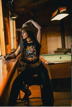 Woman in a cowboy hat and crop top posing in a bar with a pool table