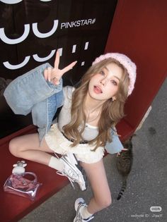 Woman in a pink beanie and denim jacket making a v sign with a cat nearby