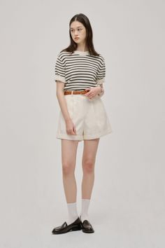 Woman in a striped shirt, white shorts, and loafers posing in a studio
