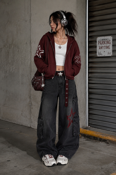 Woman in a maroon hoodie, baggy jeans, and headphones in an urban setting