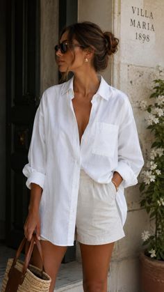 Woman in a white linen shirt and shorts holding a straw bag outdoors