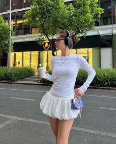 Woman in a white top and bubble skirt with headphones and sunglasses on a street