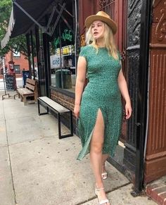 Woman in a green dress with a high slit and hat walking on a city street