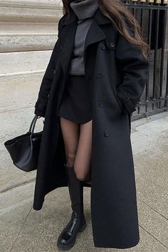 Person in a long black coat, gray turtleneck, and black mini skirt with knee-high boots