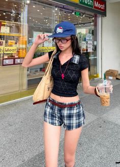 Woman in a crop top and plaid shorts holding iced coffee outdoors