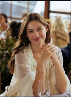 Woman with long hair wearing a white blouse and smiling at a table indoors