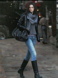 Woman in a leather jacket, jeans, and boots walking on a street