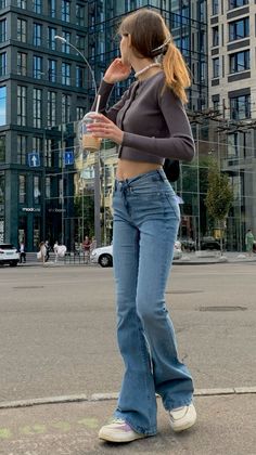 Woman in a crop top and flared jeans holding a drink on a city street