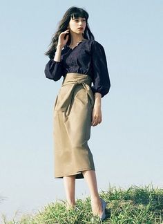 Woman with long dark hair wearing a navy blouse and a high-waisted midi skirt outdoors