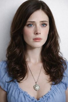 Woman with long brown hair and blue eyes wearing a blue top and necklace