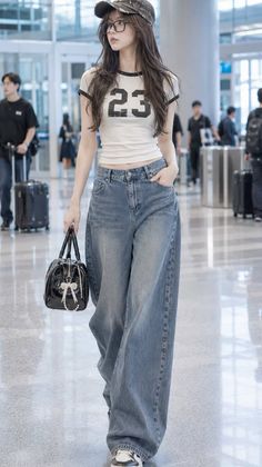 Woman in a crop top, wide leg jeans, and baseball cap walking through an airport