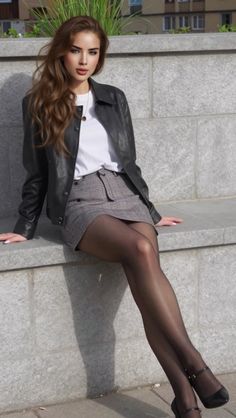 Woman with long brown hair wearing a leather jacket and mini skirt, sitting outdoors