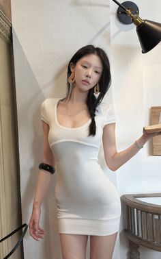 Woman in a tight white dress with a braid and earrings indoors