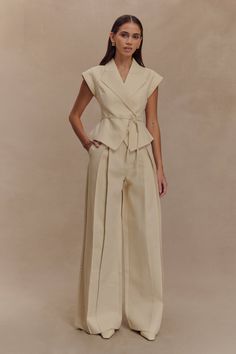 Woman in a beige peplum top and wide leg pants posing in a studio