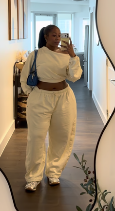 Woman in a cropped top and sweatpants taking a mirror selfie indoors