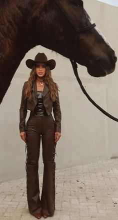 Woman in a brown cowboy hat and leather outfit standing next to a horse