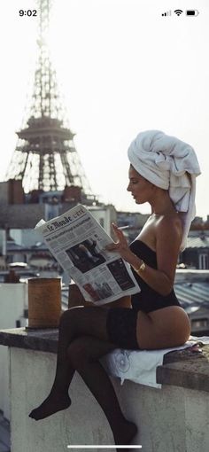 Woman in a black bodysuit and stockings reading a newspaper on a rooftop with the Eiffel Tower in the background