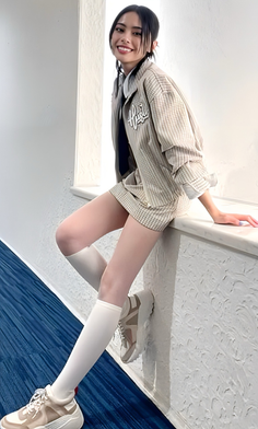 Woman in a plaid jacket and shorts sitting on a ledge indoors