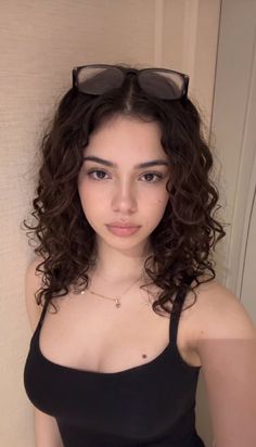 Woman with curly hair and glasses on her head wearing a black top