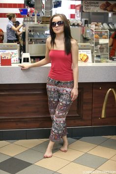 Woman in a strapless top and patterned pants standing barefoot in a fast food restaurant