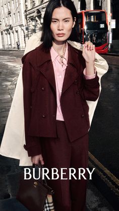 Woman in a maroon suit and striped shirt on a city street with a red bus