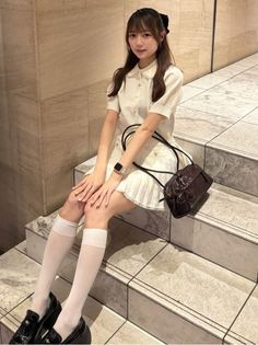Woman with long hair wearing a white dress and knee-high socks, sitting indoors