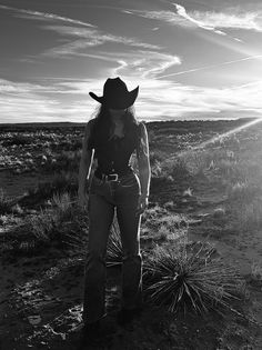 Woman in a cowboy hat and jeans standing in a desert landscape at sunset
