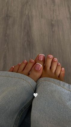 Feet with french tip pedicure resting on a wooden floor, wearing jeans