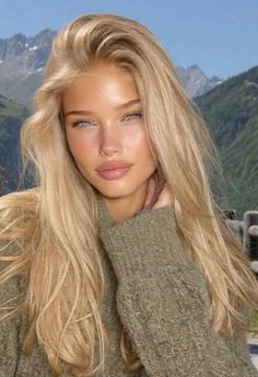 Woman with blonde hair and blue eyes in a green sweater with mountains in the background