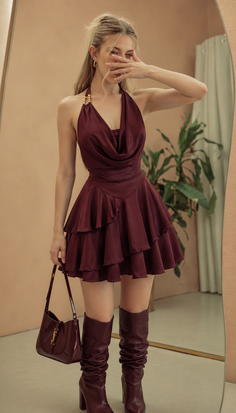 Woman in a maroon dress and high boots holding a handbag indoors