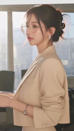 Woman in a beige blazer and glasses with her hair in an updo indoors