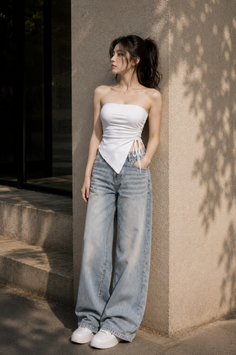 Woman in a white tube top and baggy jeans leaning against a wall outdoors
