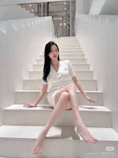 Woman in a white dress sitting barefoot on white stairs indoors