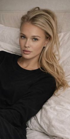 Woman with blonde hair and blue eyes wearing a black shirt, lying in bed