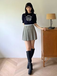 Woman in a plaid skirt and knee-high boots standing indoors