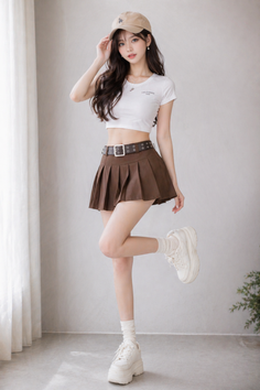 Woman in a crop top and pleated skirt posing indoors