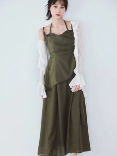 Woman in an olive green dress with white lace sleeves against a white background