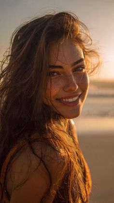 Woman with long hair and freckles smiling at the beach during golden hour