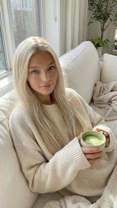 Woman with long blonde hair in a sweater holding a cup of matcha