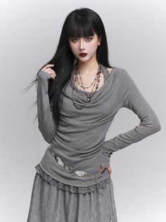 Woman with long black hair and dark lipstick wearing a gray top and skirt
