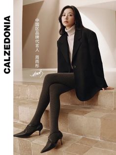 Woman in a black blazer and tights sitting on steps indoors