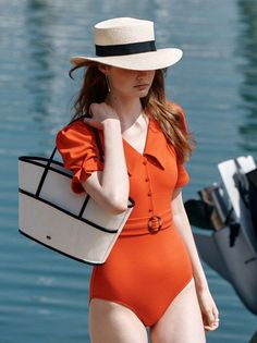 Woman in an orange swimsuit and straw hat carrying a tote bag outdoors