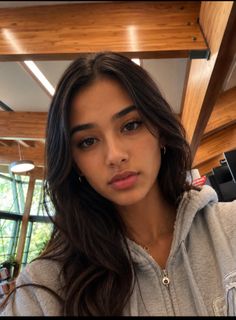 Woman with long dark hair wearing a grey hoodie and necklace indoors
