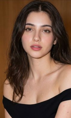 Woman with long dark hair wearing an off-shoulder top with visible cleavage