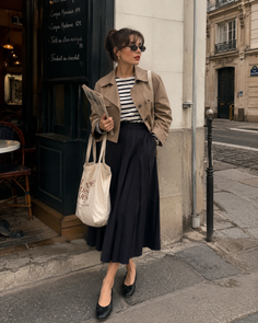 Woman in a pleated skirt and trench coat standing on a street